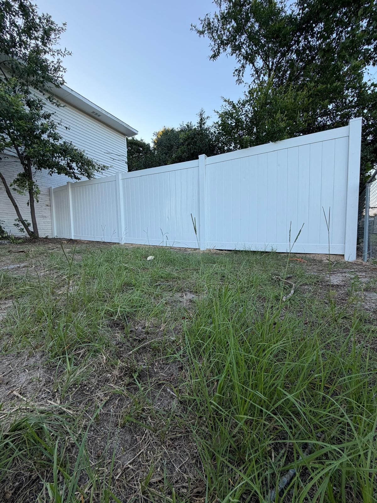 Completed white vinyl privacy fence installed by CAMINTEL beside a residential property