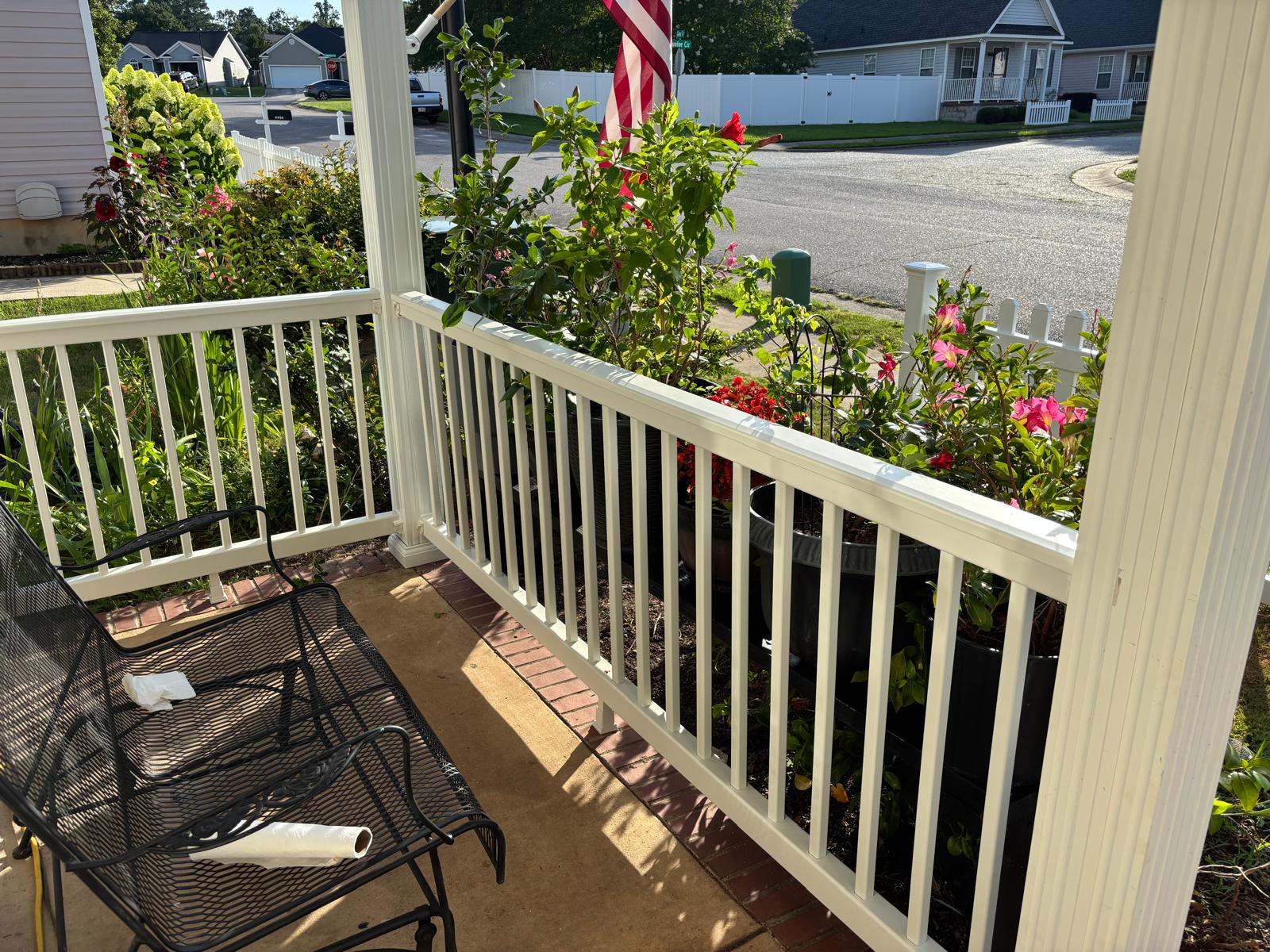 Completed white porch railing installed beside a residential garden