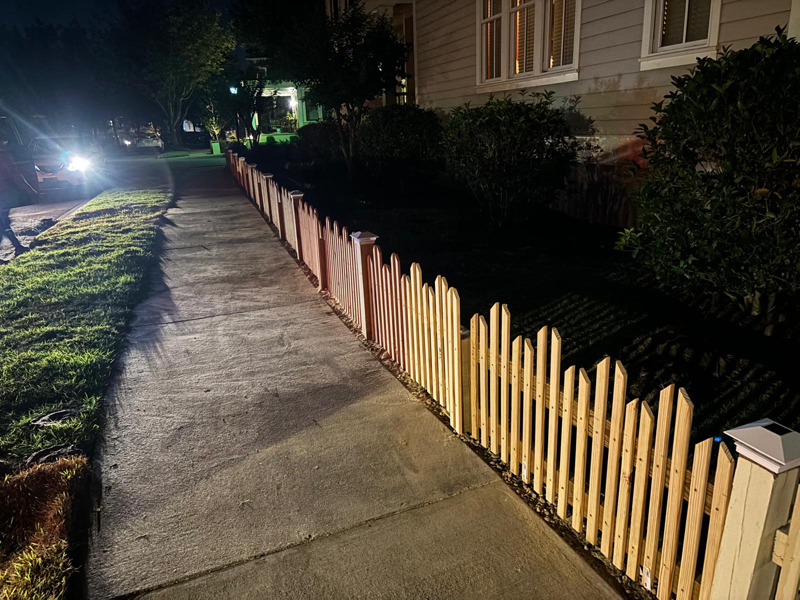 New wood picket fence installed along a residential walkway at night