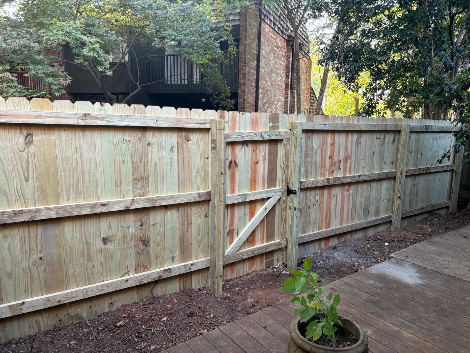 Completed natural wood privacy fence and access gate beside a deck